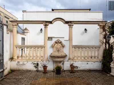 ...mentre a sinistra non passa inosservato un patio classicheggiante con una fontana centrale affiancata da due balaustre